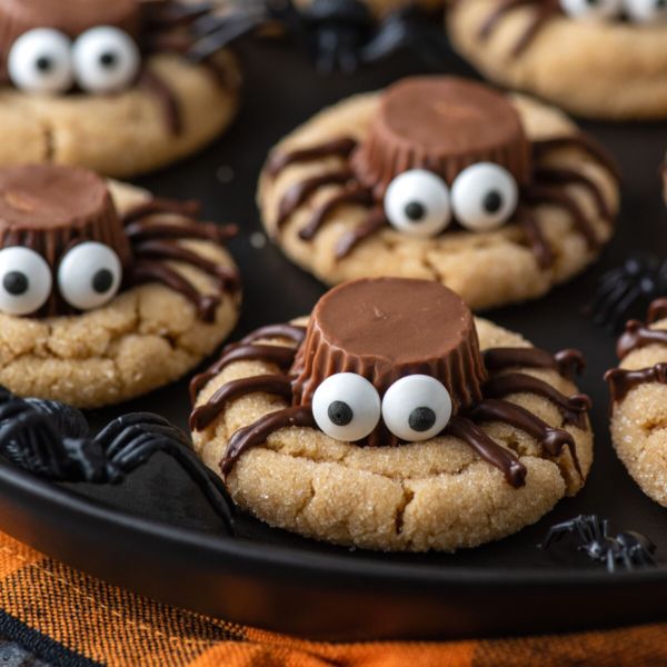 chocolate spider cookies with googly eyes on a black plate