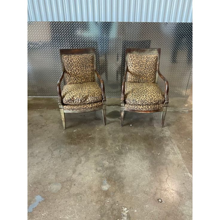 two leopard print chairs sitting next to each other in front of a metal wall with a chain link fence behind them