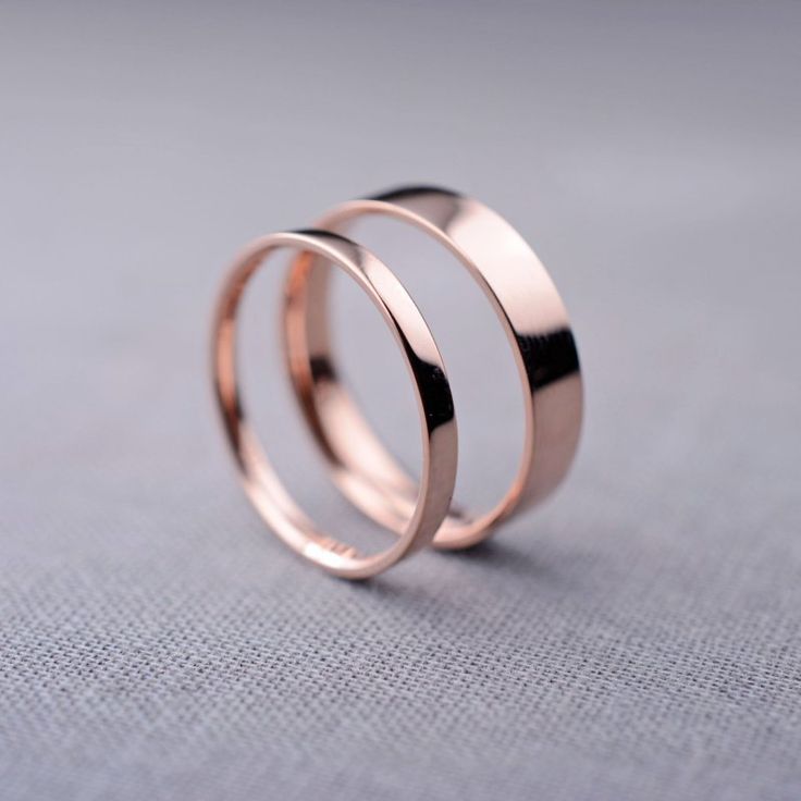 two wedding rings sitting on top of each other in front of a gray background,