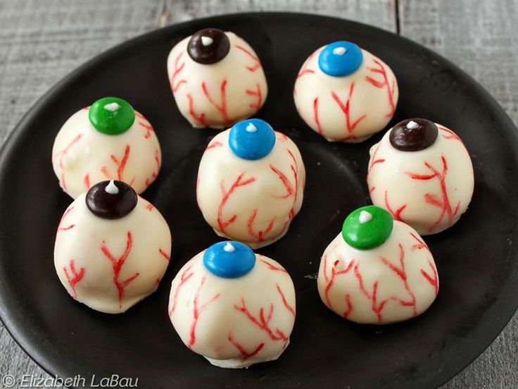 a black plate topped with white chocolate covered donuts and candy eyes on top of each other