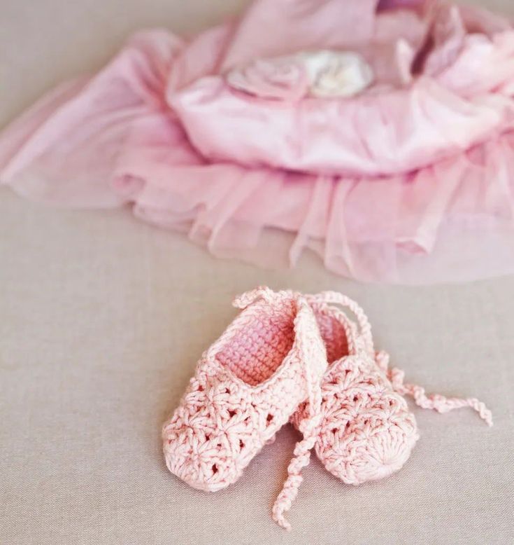 a pair of crocheted baby shoes sitting on top of a bed next to a pink blanket