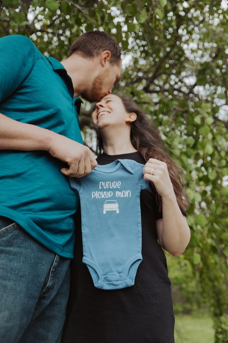 a man and woman standing next to each other holding up a baby's shirt