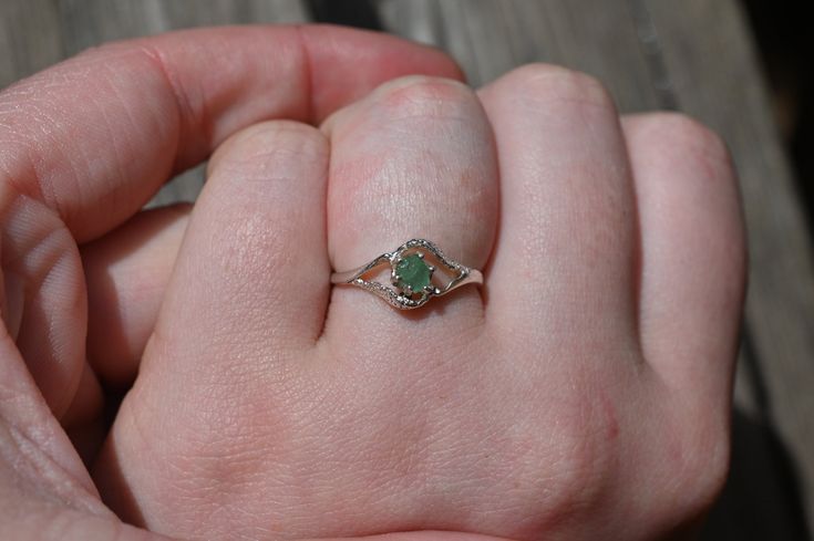 a person's hand holding a ring with a green stone