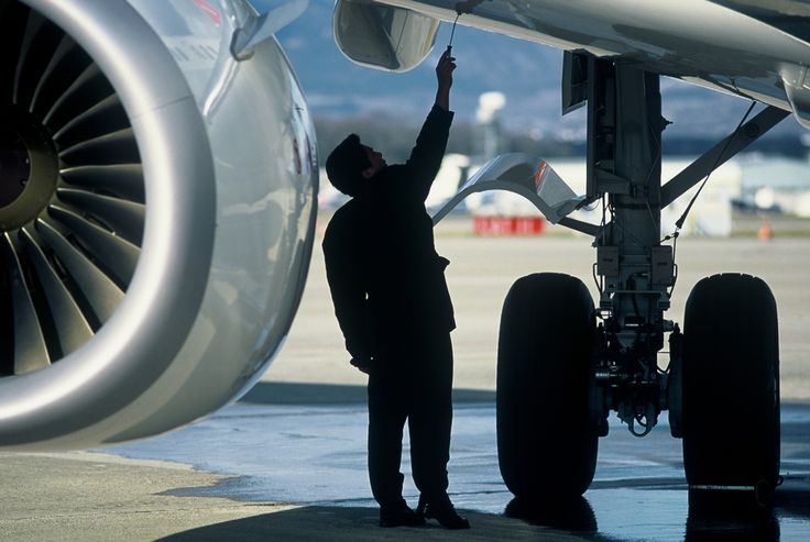 a man standing next to an airplane on the tarmac with his hand in the air