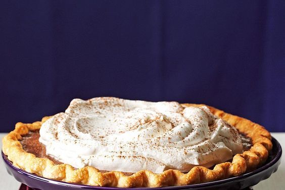 a pie with whipped cream on top sitting on a purple plate in front of a blue curtain