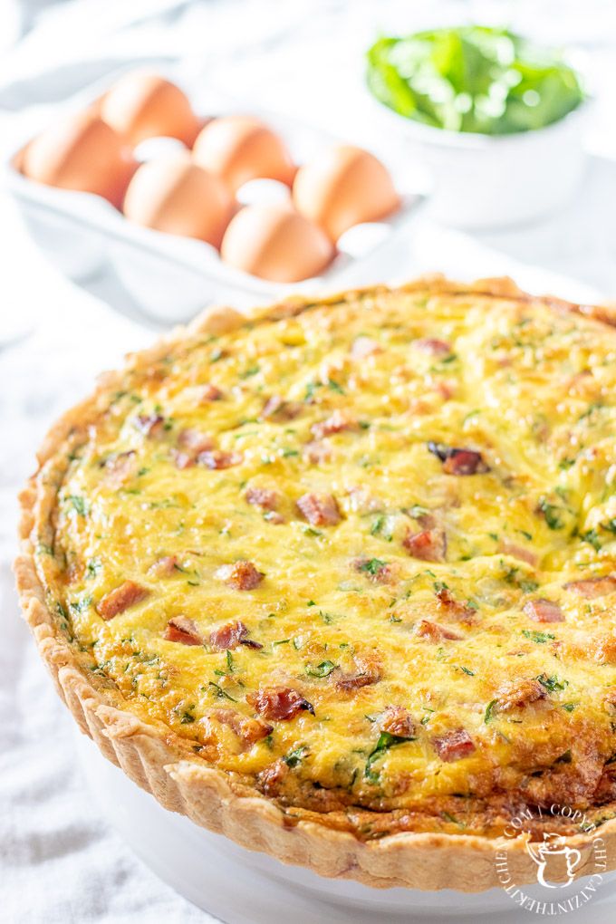 ham and cheese quiche with fresh spinach in a white dish on a table