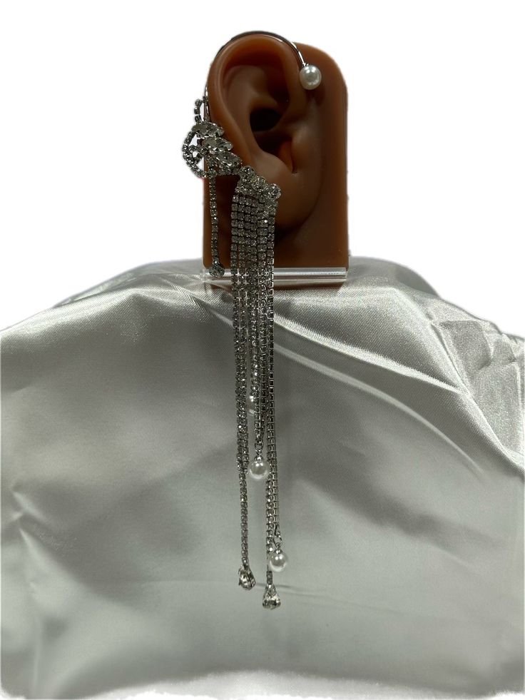 The Stellar Waterfall Ear Cuff is an exquisite piece that cascades down the ear with fluidity. Set in fine silver, it features rows of meticulously placed sparkling gems. At intervals, lustrous pearls punctuate the design, adding an element of classic elegance to the modern silhouette. This ear cuff is designed for the fashion connoisseur, a statement piece that marries the timeless allure of pearls with the daring sparkle of a starlit galaxy. Silver Cubic Zirconia Ear Cuff For Party, Silver Metal Ear Cuff For Formal Occasions, Silver Crystal Ear Cuff For Party, Elegant Metal Ear Cuff For Evening, Silver Solo Earring For Parties, Elegant Metal Ear Cuff, Silver Dangle Ear Cuff For Party, Elegant Metal Single Ear Cuff, Elegant Metal Ear Cuff For Party