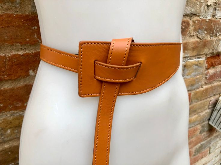 "NEW STYLE. Camel brown  OBI BELT in  genuine leather. Waist belt in soft natural leather. Saddle brown color 80s style belt. One side \"passes through\" the other through the 2 eyelets and then can be either hidden behind or passed through again at the front, please see pictures!  Available in gray, burgundy, mustard yellow, black and taupe color ( light brown-dark greyish beige) The belt is 116 cm (46 in) long   6 cm (2  1/2in) wide at one side and 2 cm ( 3/4 in) at the other side  Our genuine Chic Adjustable Brown Belt, Spring Leather Corset Belt, Leather Corset Belt For Spring, Chic Brown Leather Corset Belt, Chic Brown Corset Belt With Self Belt, Brown Fitted Leather Belt, Fitted Brown Leather Belt, Brown Leather Corset Belt With Removable Belt, Adjustable Brown Corset Belt With Matching Belt