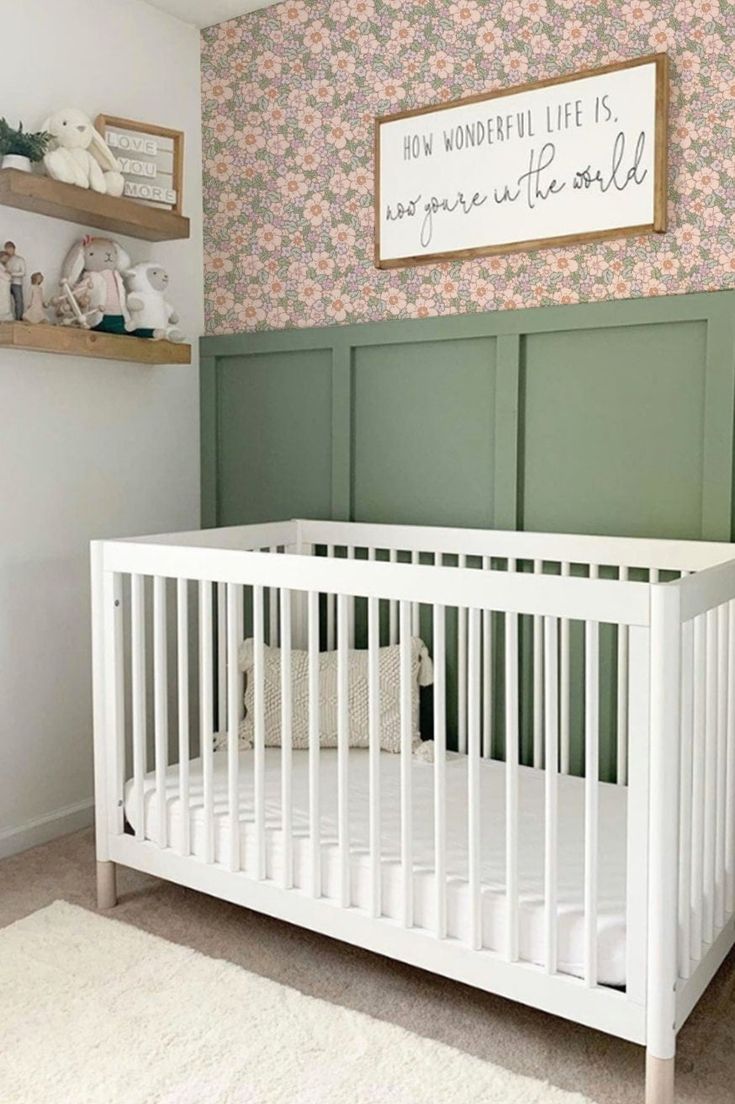 a white crib in front of a wall with green paneling and flowers on it