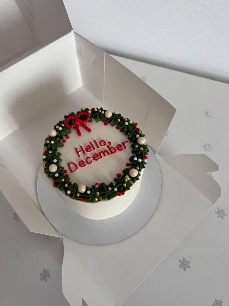 a white cake decorated with holly wreaths and red bow on top in a box