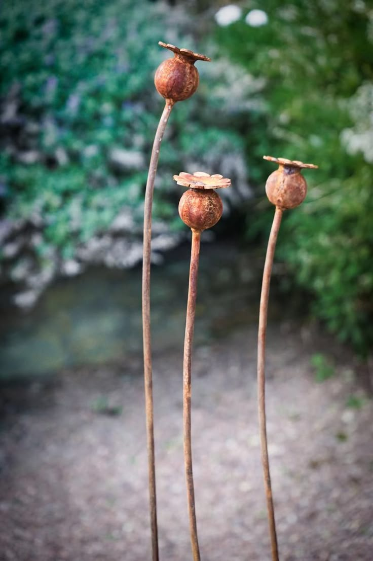 three rusted metal flowers in front of some bushes