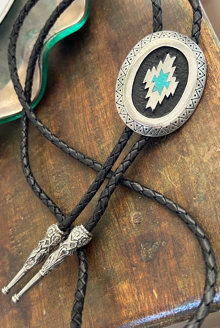 This awesome bolo tie has a southwestern design and real turquoise stone inlay. The cord is genuine leather. Measurements/Sizing Total length of leather is approx. 40 inches1 1/4'' x 2 1/4'' in pendant Handmade Artisan Bolo Ties For Western-themed Events, Hand Tooled Western Bolo Ties As Gift, Western Style Hand Tooled Bolo Ties As Gift, Adjustable Southwestern Bolo Tie For Western-themed Events, Handmade Southwestern Lariat Bolo Tie, Western Style Concho Jewelry As Gift, Artisan Hand-tooled Jewelry For Rodeo, Western Style Concho Jewelry For Gift, Southwestern Style Adjustable Bolo Ties