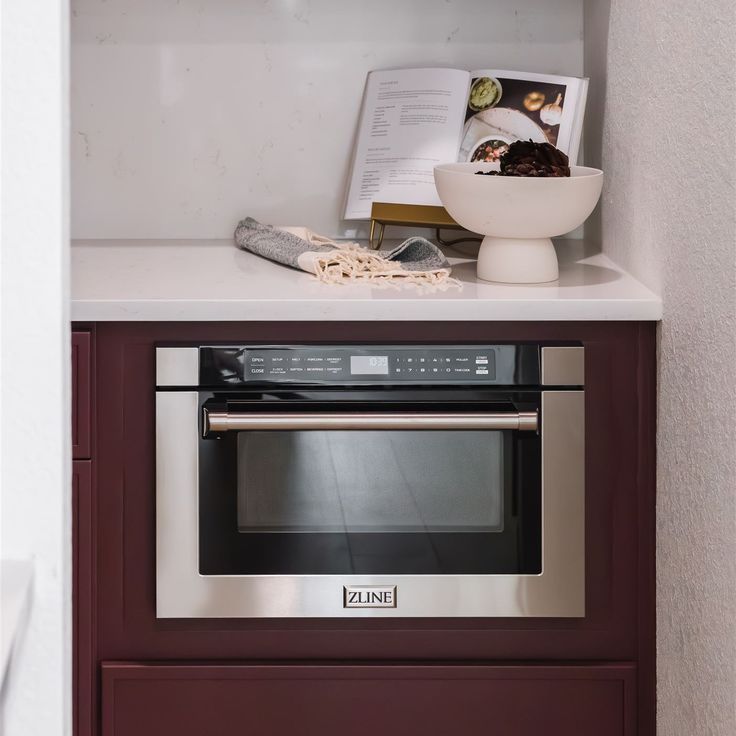 a microwave oven sitting on top of a counter next to a bowl of cereal and an open book