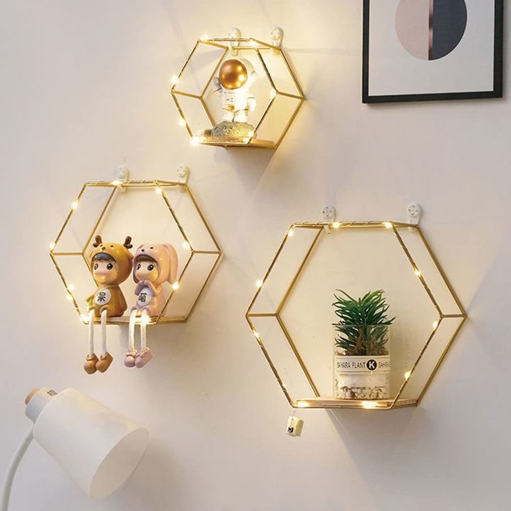 three gold hexagonal shelves on the wall with plants and toys hanging from them