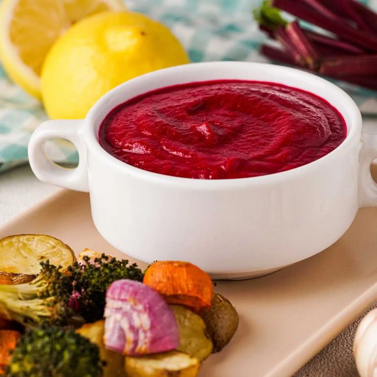 a white bowl filled with red sauce next to vegetables