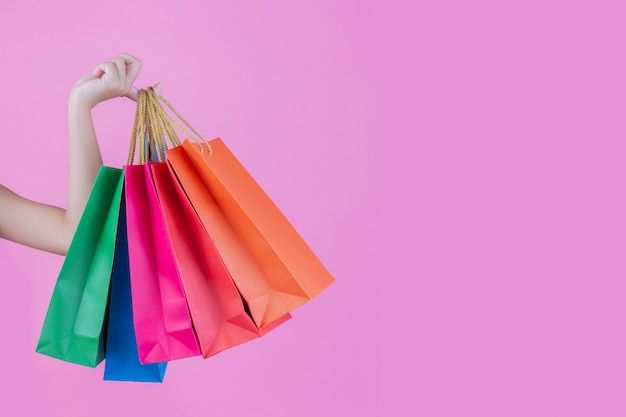 a woman is holding several shopping bags in her hand and looking at the camera on a pink background