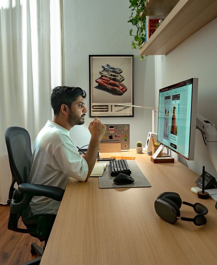 a man sitting in front of a computer desk with headphones on his ears and looking at the monitor