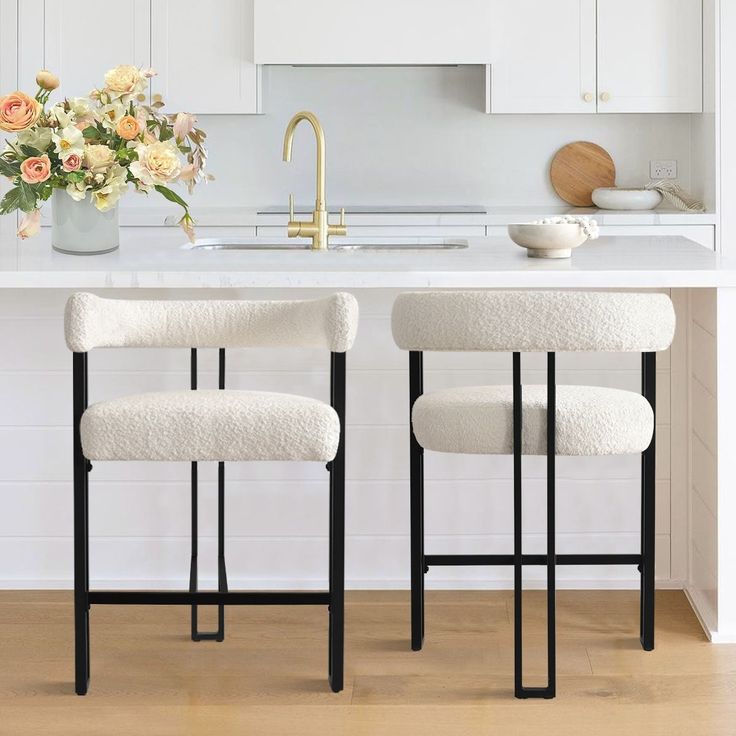 two white stools sitting in front of a kitchen counter with flowers on the island