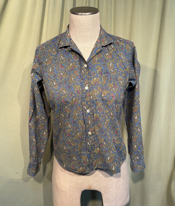 This is an adorable vintage blouse from the 50s or so. Labeled Lady Sutton. Tagged a size 36. The bust measures 36" with measurements below. Made of a blue & green cotton in a paisley print. The blouse closes down the front with plastic buttons. The blouse has long sleeves with button cuffs. Hem is a slight curved shirttail hem.   The blouse is in very good condition!  No damage. No stains or soil. Super cute!  If you have never worn vintage before, please measure yourself!! Vintage sizes run smaller than today's sizes, know your measurements before buying! Bust measured from side seam to side seam at the underarm: 18" for a 36" or smaller bust Hemline from side seam to side seam: 17" for a 34" hemline Shoulders: 15" Length measured from shoulder to hem: 19.5 Sleeve from underarm: 18.5 Classic Paisley Print Tops For Fall, Fitted Paisley Print Button-up Top, Classic Patterned Top With Paisley Print, Classic Paisley Print Patterned Tops, Classic Patterned Tops With Paisley Print, Classic Blue Paisley Print Tops, Vintage Paisley Print Button-up Top, Vintage Button-up Top With Paisley Print, Fitted Button-up Paisley Print Blouse