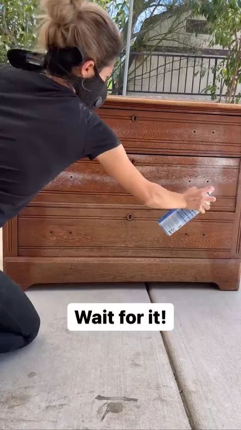 a woman in black shirt and face mask cleaning wooden furniture with a spray bottle on it