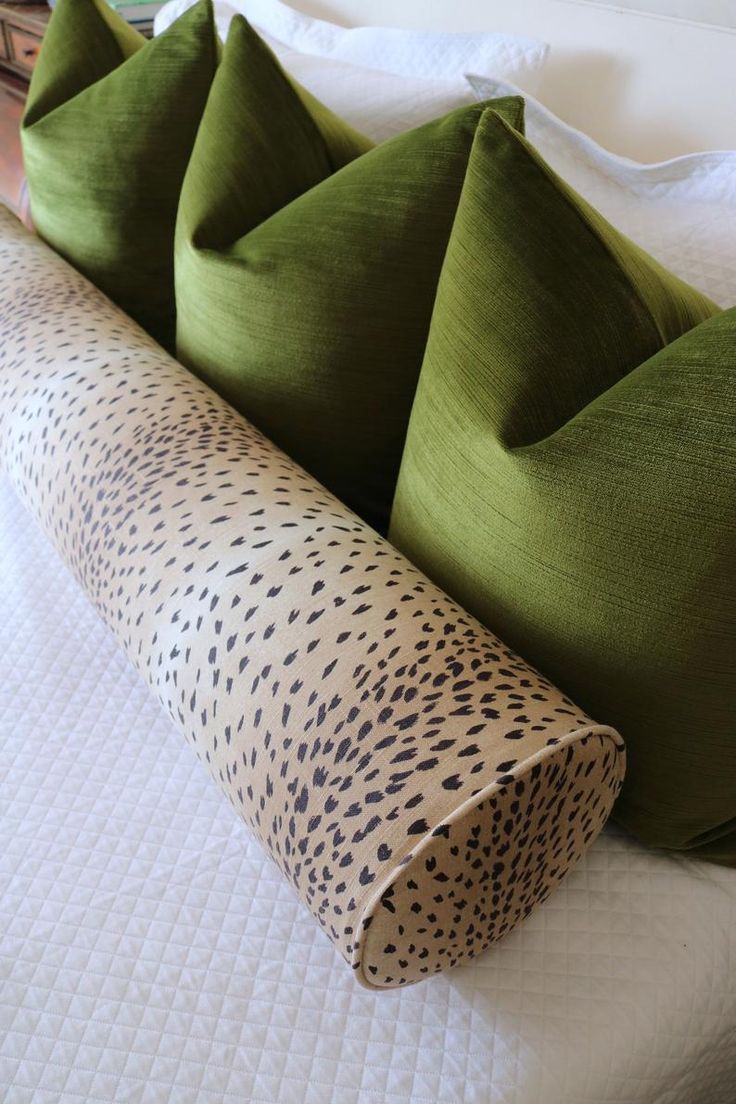 four green pillows on top of a bed with white sheets and pillow cases in the shape of cheetah spots