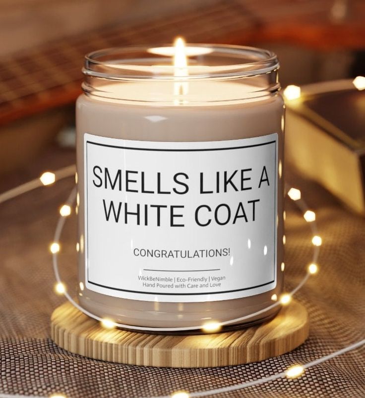 a candle that says smells like a white coat on top of a wooden coaster with lights around it