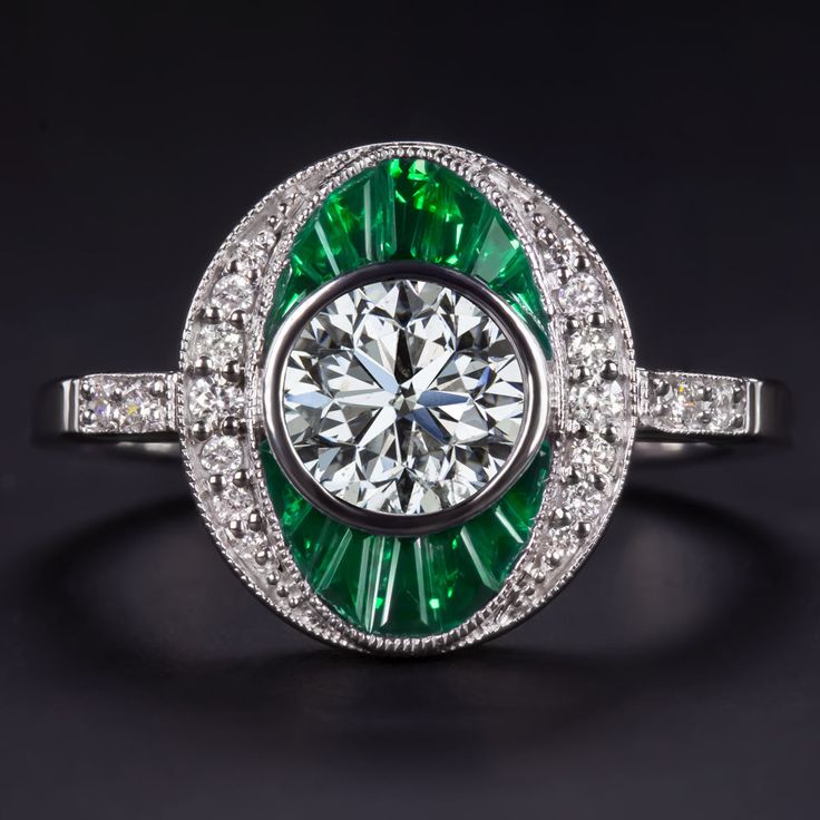 an emerald and diamond ring on a black surface with diamonds around it, in white gold