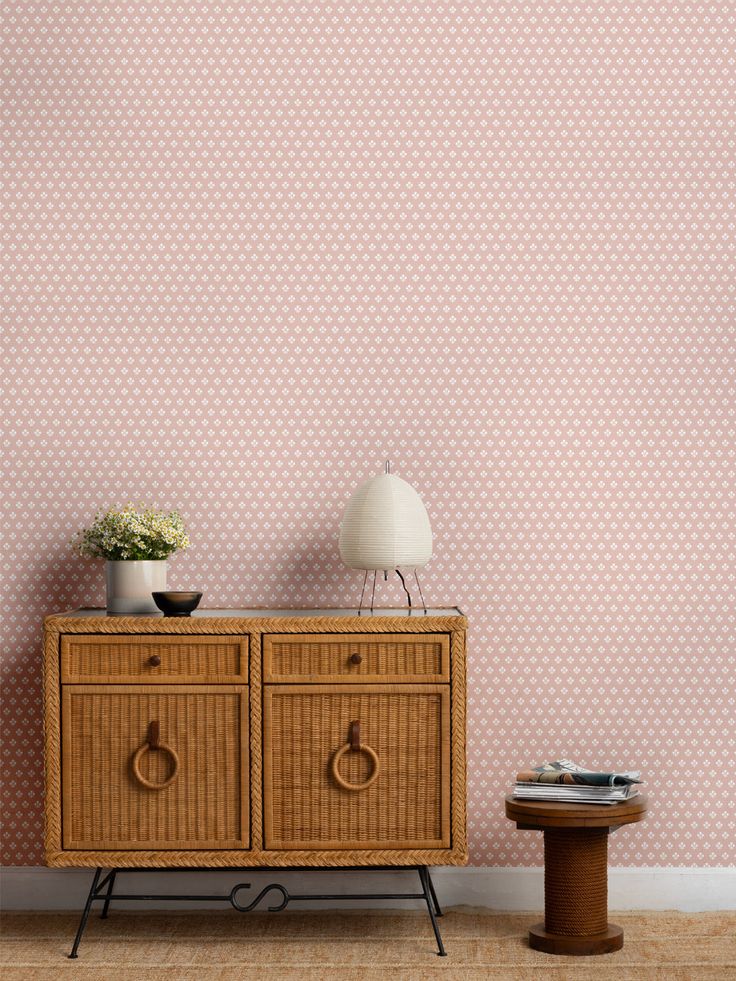 a sideboard with two drawers in front of a pink wallpapered background and a small end table