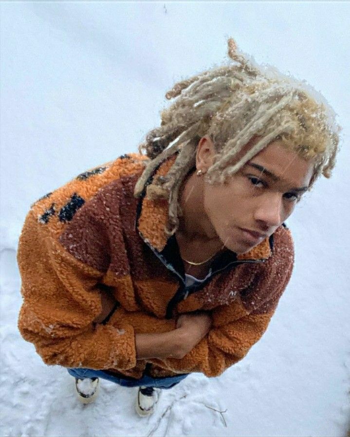 a man with dreadlocks standing in the snow wearing an orange and brown jacket