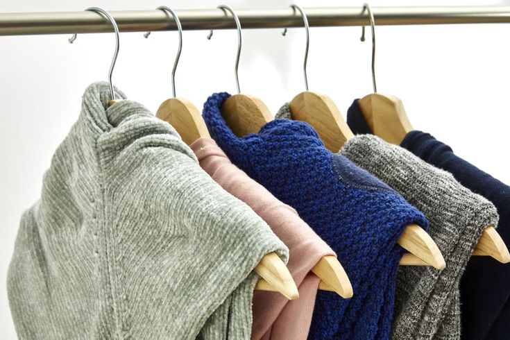 four sweaters hanging on a clothes rack with wooden hangers in front of them