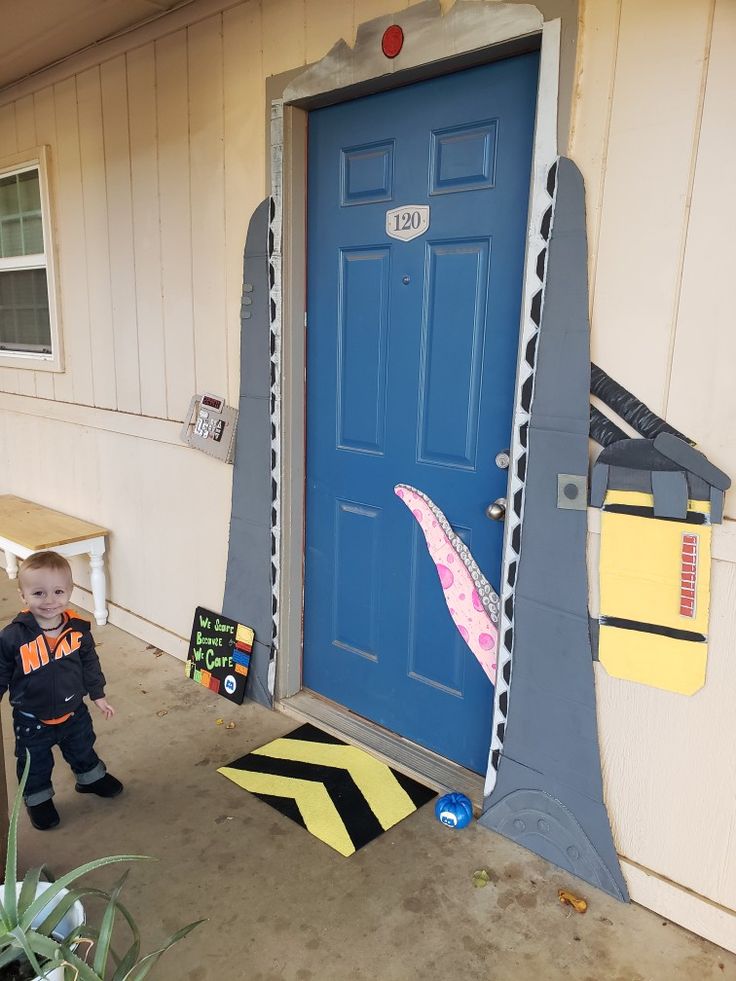 a little boy standing in front of a blue door that has a shark on it