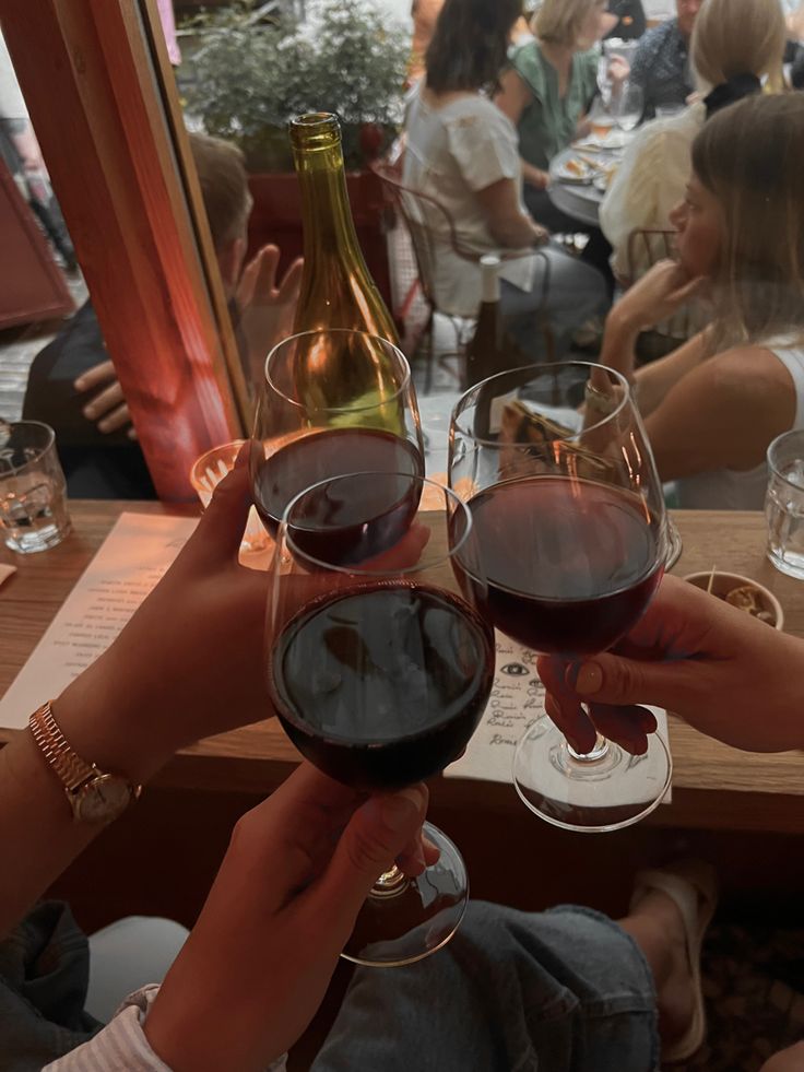 two people toasting with red wine in front of them at an outdoor dining area