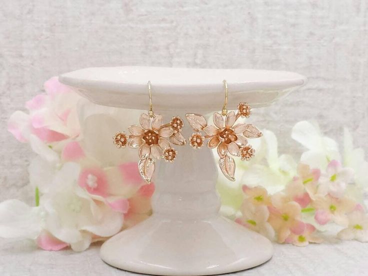 a pair of gold flower earrings sitting on top of a white pedestal next to flowers