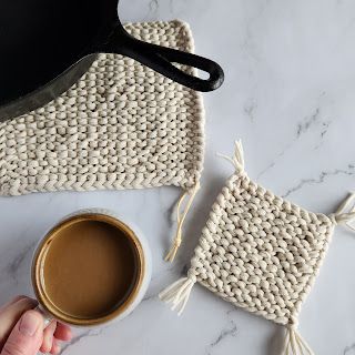 a person holding a cup of coffee next to some crocheted placemats