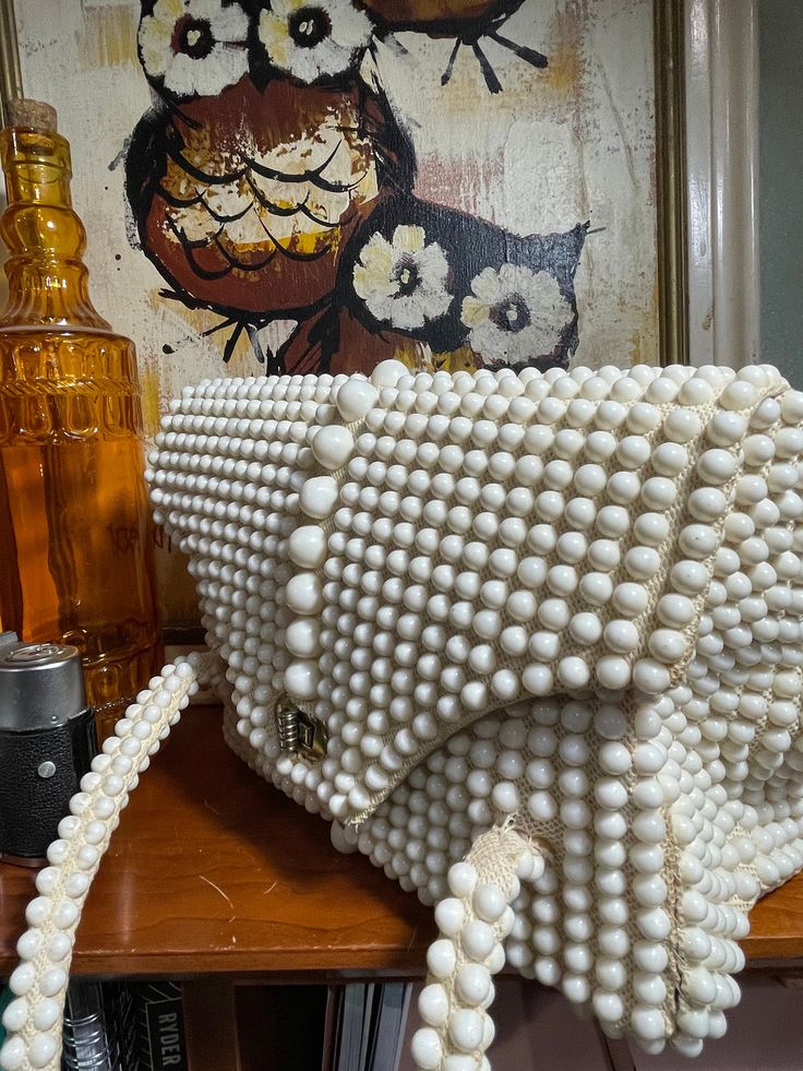 a handbag made out of pearls on a table next to a bottle and an owl painting