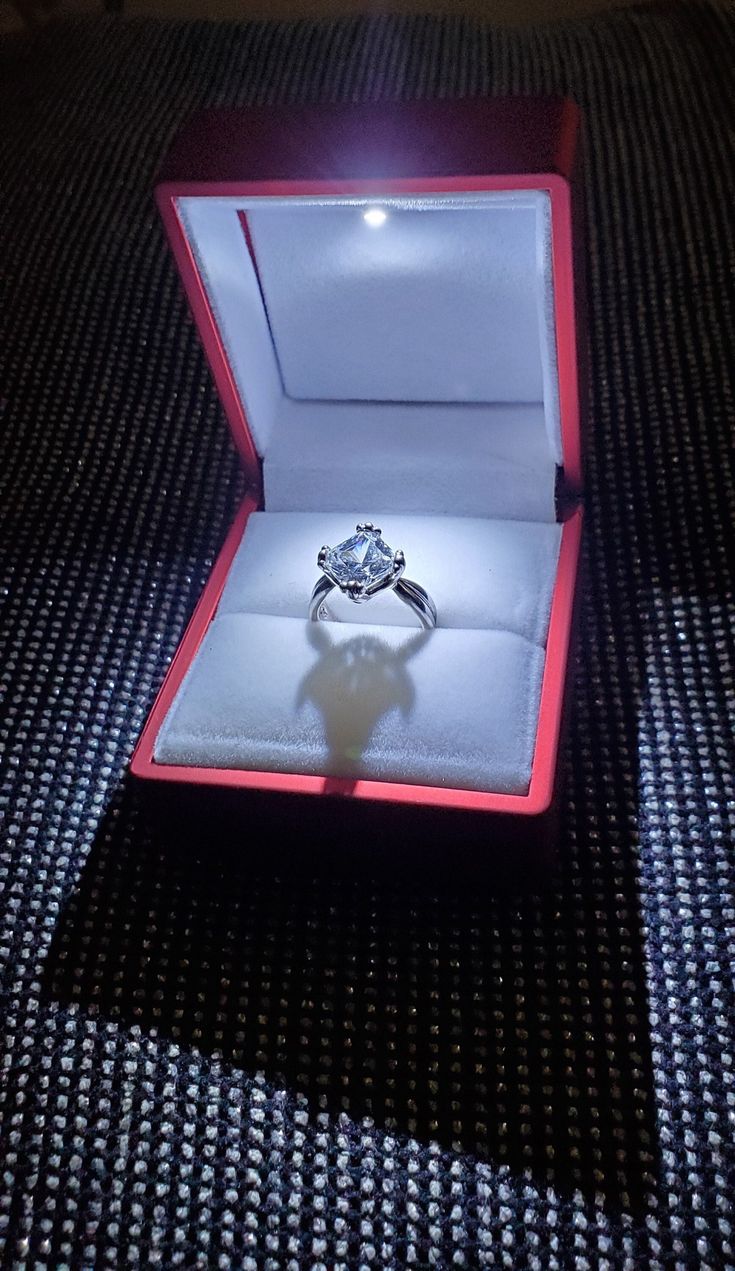 a diamond ring in a red box on a black surface with the light shining through it