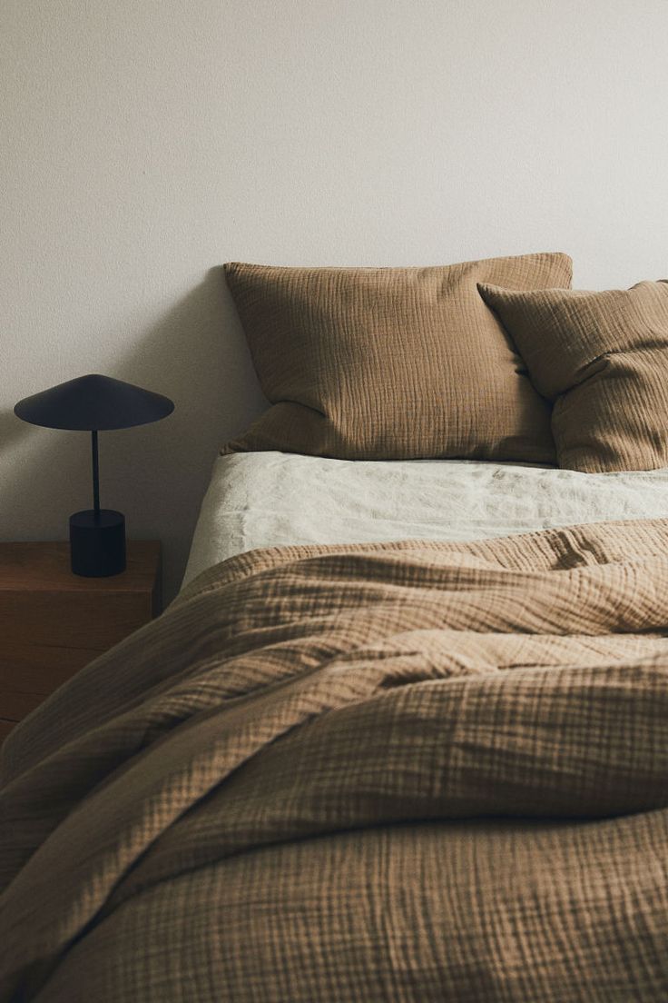 an unmade bed with two pillows and a night stand in the corner next to it