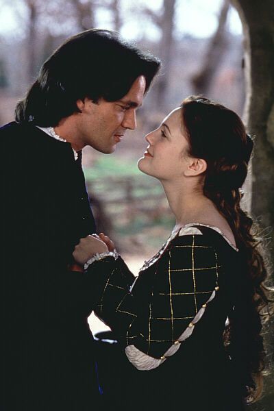 a man and woman standing next to each other in front of a tree with their faces close together