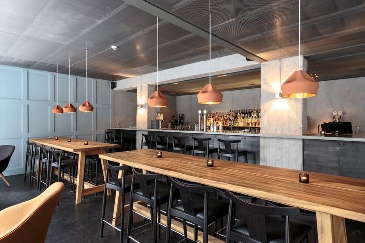 an empty bar with wooden tables and chairs in front of the bar area is lit by pendant lights