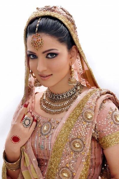 a woman in a pink and gold bridal outfit posing for the camera with her hands on her head