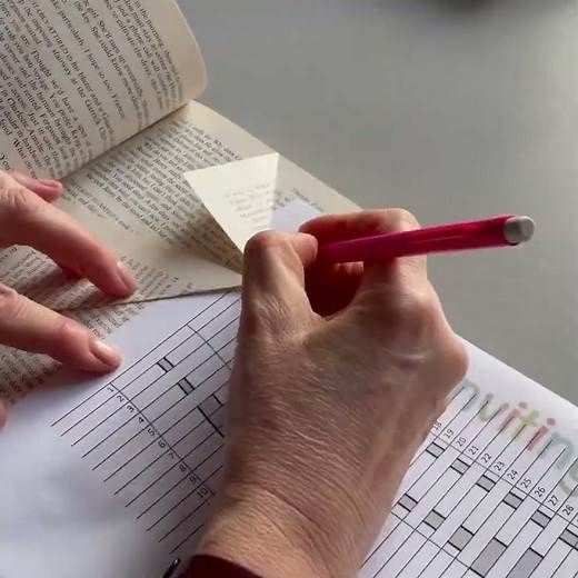 a person is holding a pencil and writing on some paper with an open book in the background