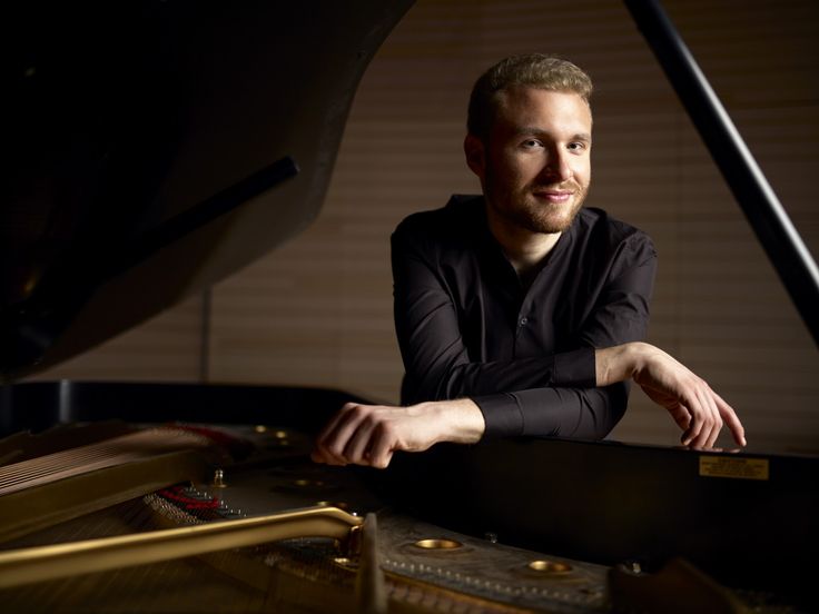 a man sitting at a piano with his hands on the keyboard and looking into the camera