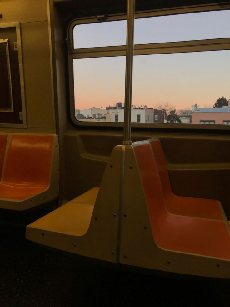 an empty train car with red seats and a view of the city from it's windows