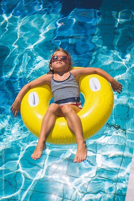 a young boy floating on an inflatable raft in a swimming pool while wearing sunglasses