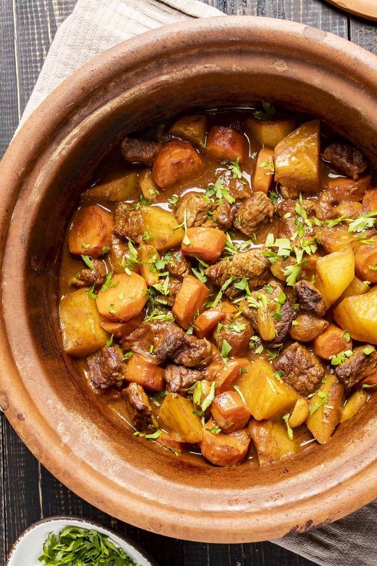 a large pot filled with stew next to a plate of bread and vegetables on a wooden table