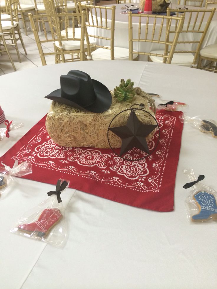 a table topped with a red bandana and black cowboy hat on top of a hay bale