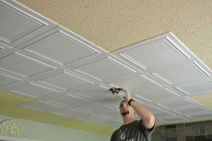 a man working on a ceiling in a living room with white tiles and light fixtures