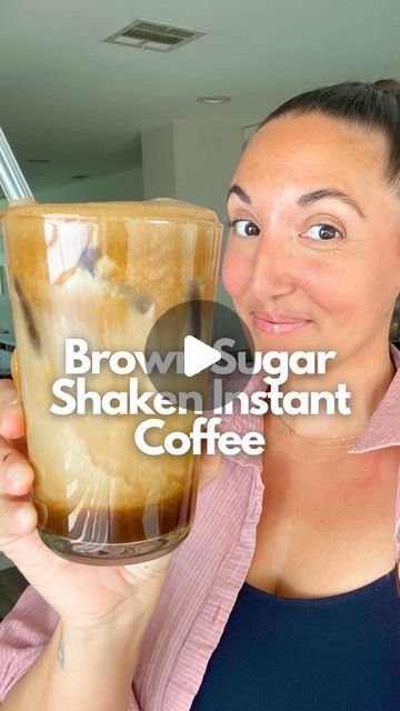 a woman is holding up a cup of brown sugar shaker instant coffee in front of her face