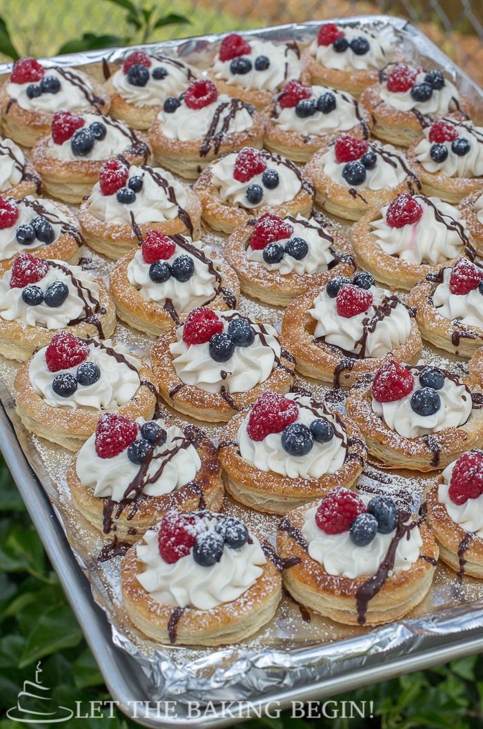 a tray filled with pastries covered in berries and whipped cream on top of each other