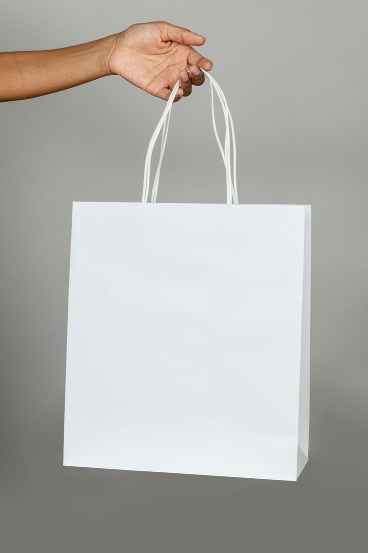 a person's hand holding a white shopping bag against a gray background with copy space